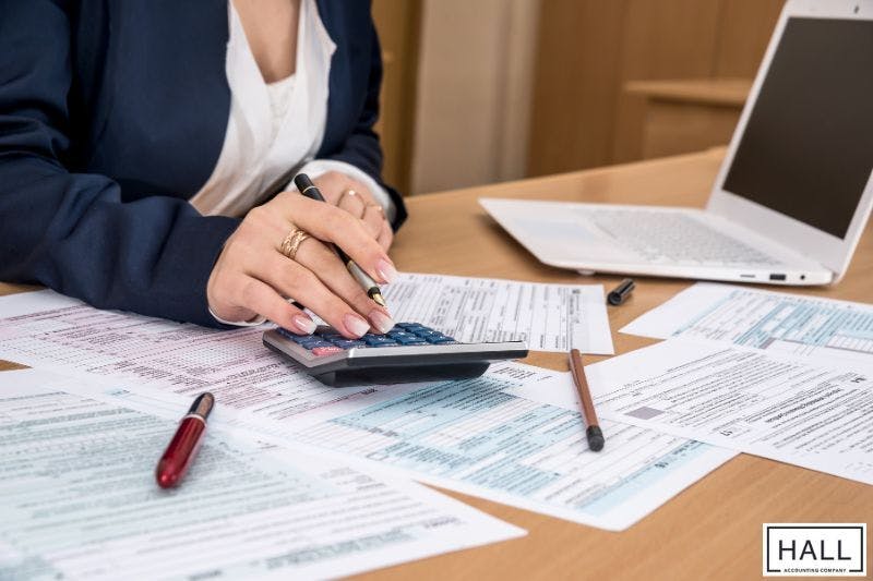A person uses a calculator while reviewing multiple tax documents on a desk.