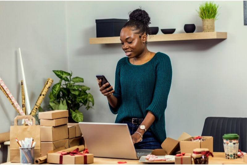 Busy woman multitasking with phone and laptop overwhelmed by bookkeeping tasks