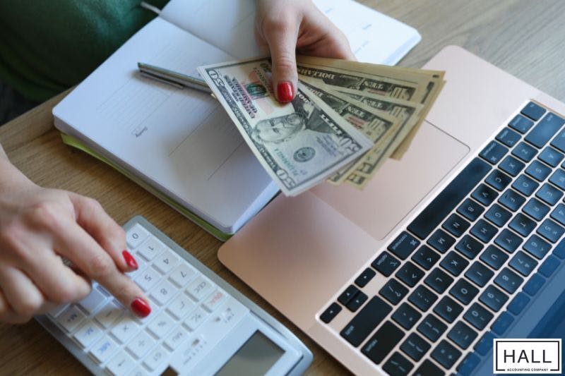 Close-up of a person managing finances with cash, a calculator, and a laptop, emphasizing proactive tax planning to protect wealth effectively.