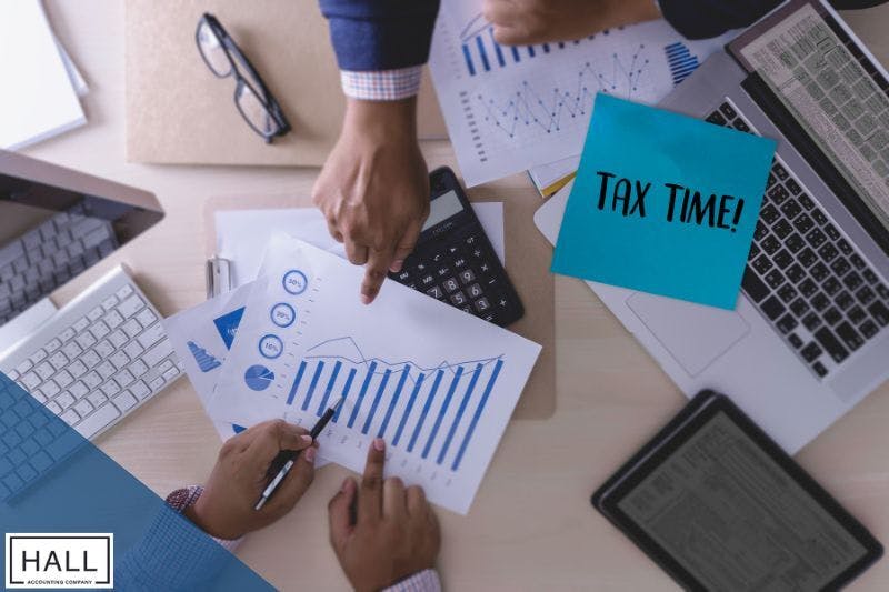 Hands reviewing financial charts with a calculator, laptop, and 'Tax Time!' note, emphasising strategic tax planning with a CPA