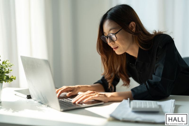 A woman working on tax calculations at a desk with a laptop, calculator, and financial documents