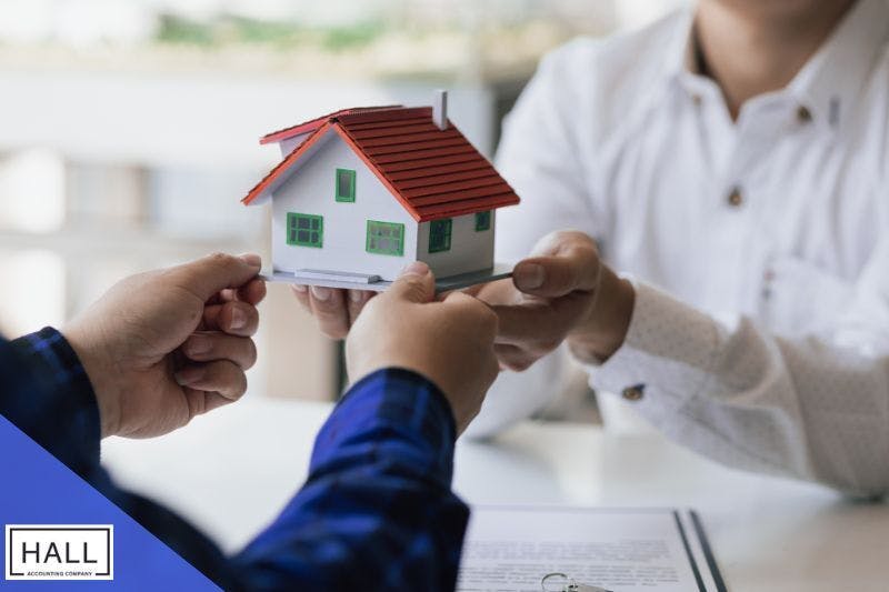 Two individuals exchanging a miniature model house in an office setting, symbolising the concept of estate planning