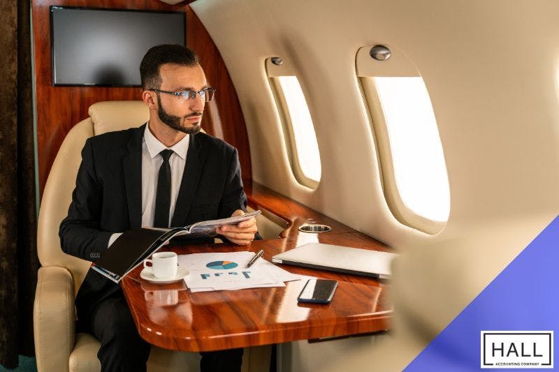 A well-dressed businessman sits in a private jet, reviewing financial documents