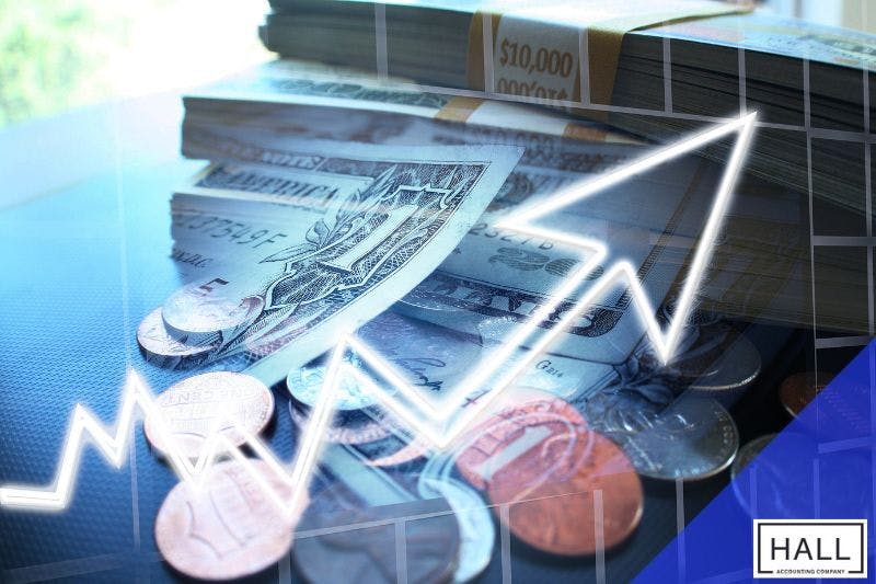 A stack of U.S. dollar bills with a white arrow pointing upward, symbolizing financial growth