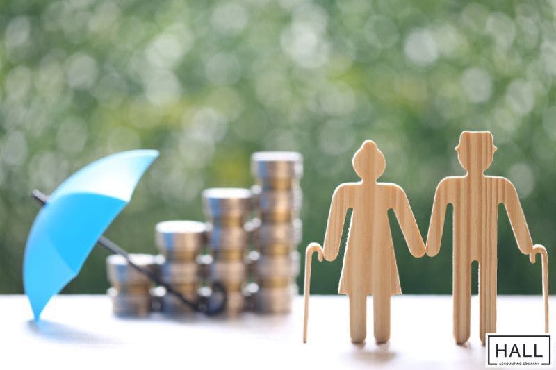 Wooden elderly figures, stacked coins, and an umbrella symbolizing