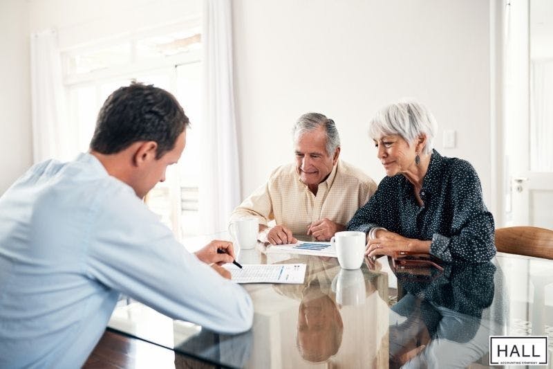 An elderly couple sits at a table with a financial advisor offering guidance on estate planning and tax return filing.