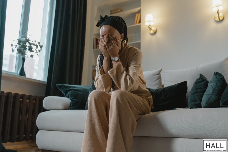 A woman sits on a couch, covering her face with her hands in a gesture of distress related to estate matters