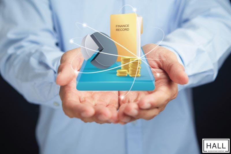 A person's hands cupping a 3D model of a financial record book, a pie chart, and a stack of coins.