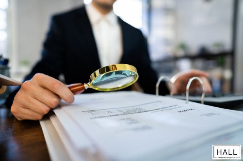A professional in a suit holds a magnifying glass over documents on a desk, indicating a detailed review process of amending a tax return.