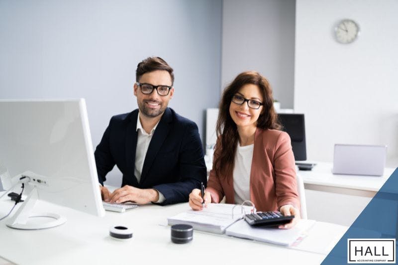 Two professional accountants smiling at their desks, working with financial documents and a calculator, representing expertise in buying tax lien properties in Texas.