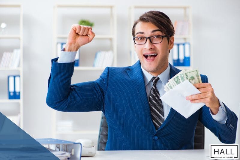 A happy businessman in a suit holds cash and an envelope, celebrating his earnings in an office