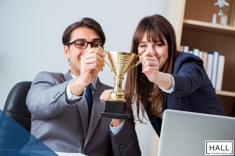 Two happy professionals in an office celebrate success, holding a golden trophy, symbolizing financial rewards and bonuses