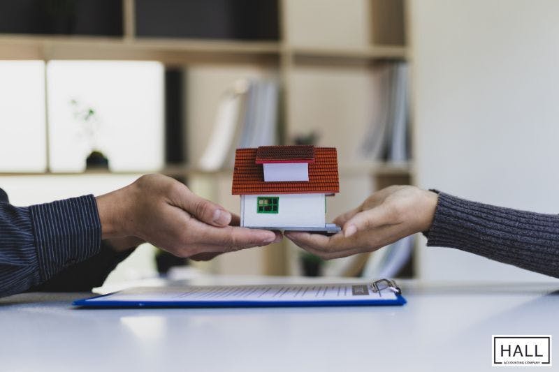 A person's hands carefully transferring a small model house to another person's hands, symbolizing the gifting of real estate as a strategy to potentially reduce federal estate taxes