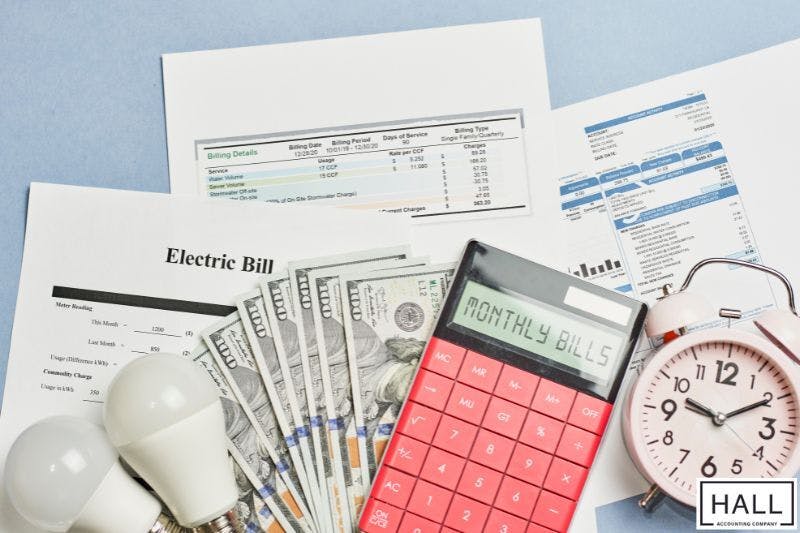A photo of utility bills with calculator, clock, and loose change on a table.