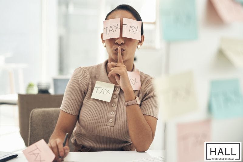 A person, seated at a desk, holds a finger to their lips in a