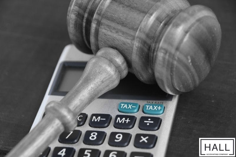 A wooden gavel rests on top of a calculator's displaying the words