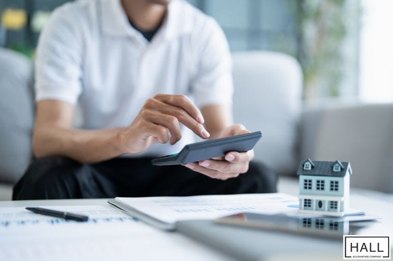 Man using calculator beside house model and documents, representing sales tax in San Antonio, Texas.