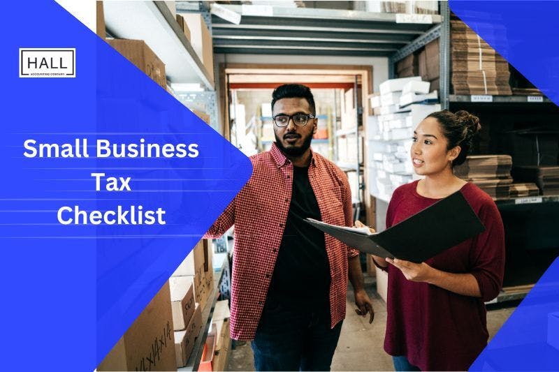 Two small business owners are standing in a warehouse, discussing Business Tax while holding a clipboard