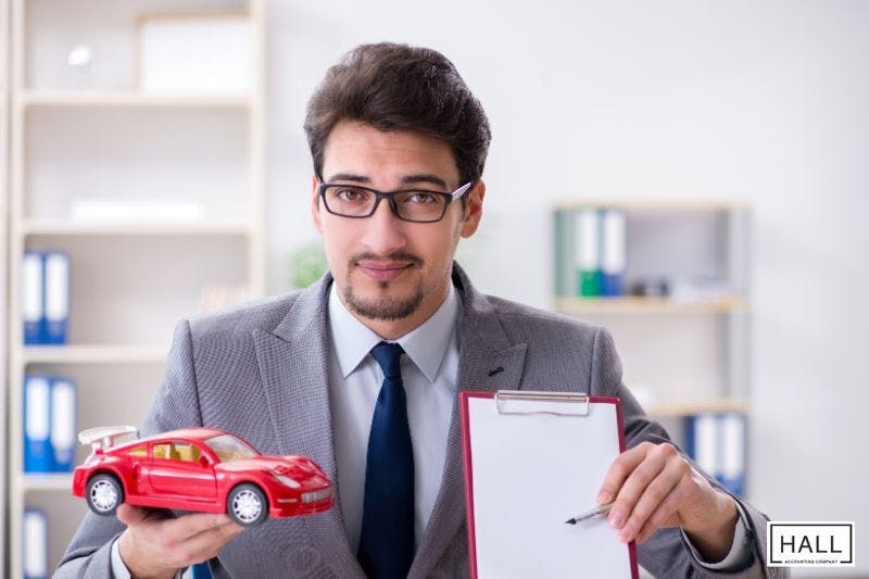 A suited man holds a toy car and clipboard, explaining tax deductions or vehicle-related expenses for business tax preparation.