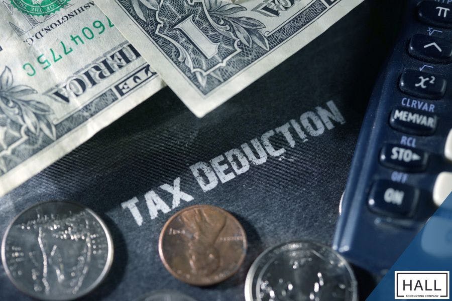 Close-up of cash, coins, and a calculator on a surface labelled 'Tax Deduction,' representing financial planning and year-end tax preparation for small businesses.